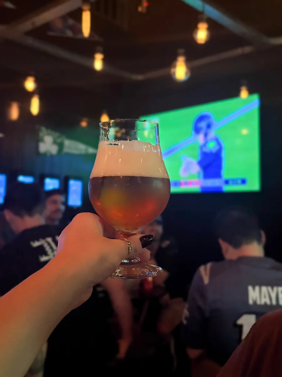 Taça de chope erguida em frente a um telão